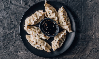 Asian dumplings with soy sauce and sesame seeds on black background. Black table setting. Copy space