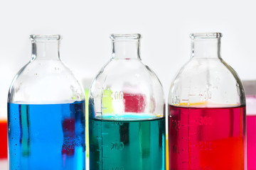 Glass bottles and flasks of different sizes with liquids of different colors on the background....