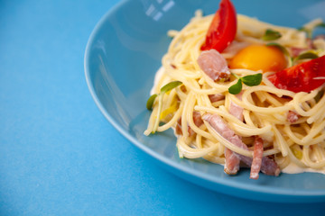 Carbonara pasta - spaghetti with small pieces of bacon, mixed with sauce of eggs, parmesan cheese. Blue plate on a blue background. Macanons with egg, tomato and meat. Italian Cuisine. Home food.