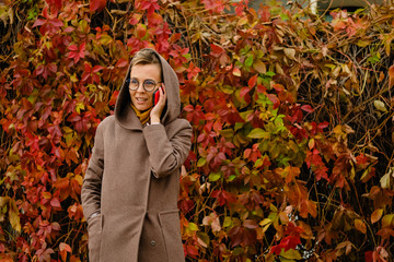 Beautiful girl in a trench coat and glasses talking on the mobile phone to the autumn background.