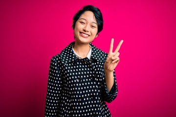 Young beautiful asian girl wearing casual jacket standing over isolated pink background showing and pointing up with fingers number two while smiling confident and happy.