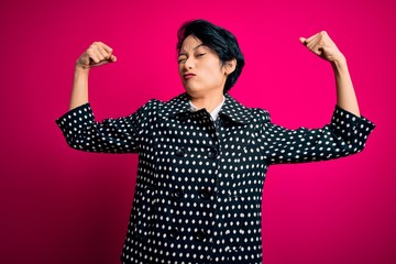 Young beautiful asian girl wearing casual jacket standing over isolated pink background showing arms muscles smiling proud. Fitness concept.