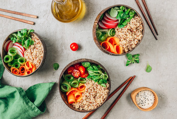 Vegan Buddha bowl. Healthy meal quinoa, tomato, cucumber, carrot, radish, corn salad in coconut bowls on concrete background.