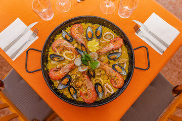 Top view of paella with seafood in a paella pan on an orange background with copy space