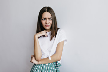 Obraz premium Unhappy woman looking away while posing on white background. Indoor shot of brown-haired female model standing in studio in trendy outfit.