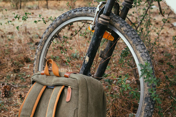 Close up of a dirty mountain bike tire with a vintage backpack near. Outdoors.