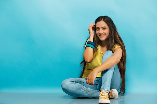 Smiling teenage girl in jeans and t-shirt sitting on the floor and posing for photograph
