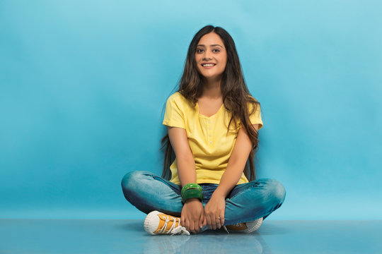 Smiling teenage girl in jeans and t-shirt sitting cross legged on the floor holding her leg
