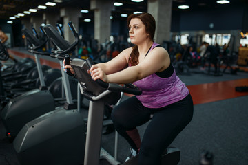 Fototapeta na wymiar Overweight woman trains on exercise bike in gym