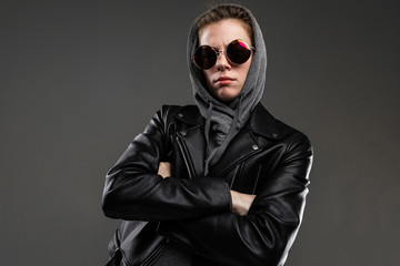 Brutal caucasian girl with rough facial features in a black jacket with a hood isolated on black background