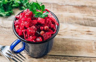 Russian traditional beetroot salad with beetroot, potato, carrot, cucumber, pea and oil dressing. Beet salad in an enameled mug over wooden background.