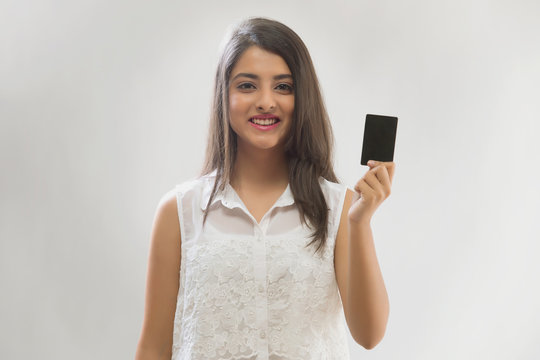 Portrait of a smiling teenage girl holding a credit card with her fingers vertically
