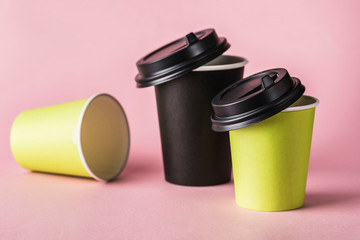 Some green and black paper reusable coffee cups with lids on a pink background.