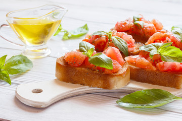 Bruschetta with tomatoes and basil on a white wooden board
