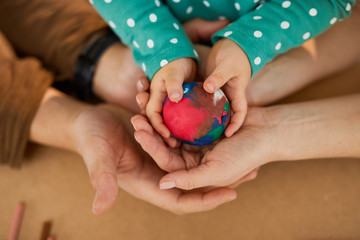 Colourful modelling clay ball in hands of child and parents, horizontal from above shot