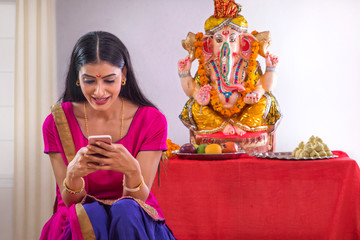 Naklejka premium Woman sitting in front of Ganesh Idol using mobile phone 