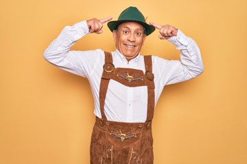 Senior grey-haired man wearing german traditional octoberfest suit over yellow background smiling pointing to head with both hands finger, great idea or thought, good memory