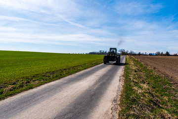 Fototapeta na wymiar road along which goes an old tractor on wood with green fields around and blue sky