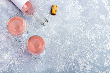 Rose wine tasting layout. Opened bottle and two glasses with rose wine on a grey background. Drunkenness concept. Top view, flat lay,  copy space for text