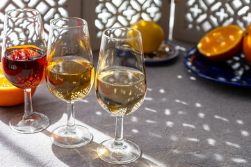 Glasses with cold dry fino and sweet cream sherry fortified wine and orange in sunlights, andalusian style interior on background