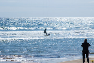 A man whatching how another is kite flyinging in the ocean
