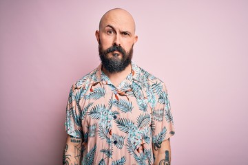 Handsome bald man with beard and tattoo wearing casual floral shirt over pink background looking sleepy and tired, exhausted for fatigue and hangover, lazy eyes in the morning.