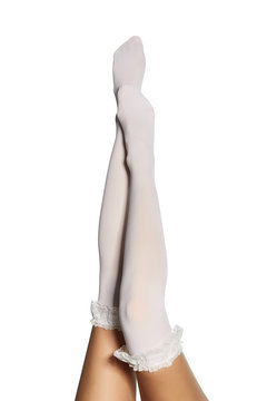 Cropped subject shot of lifted female legs in white shadow-proof stockings with ruffles on the top. The photo is made on the white background. 