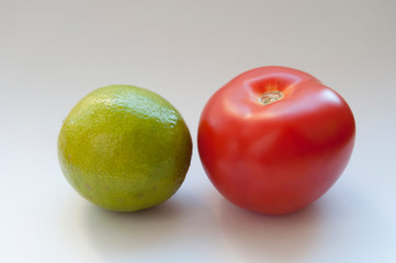 one red tomato and a green lime on a white background