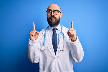 Handsome bald doctor man with beard wearing glasses and stethoscope over blue background Pointing...