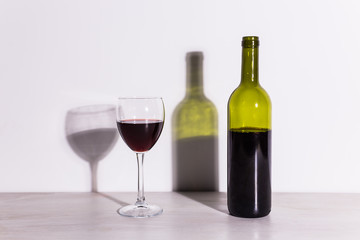 A glass of wine and a bottle casts a long shadow from the evening sun.