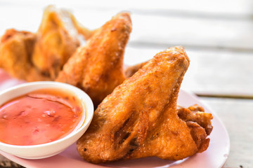 Thai style homemade fried chicken wings on white plate.A plate of fresh, hot, crispy fried chicken..Fried chicken wings with spicy Thai dip sauce..Crispy fried chicken on the table.