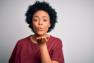 Young beautiful African American afro woman with curly hair wearing casual t-shirt standing looking at the camera blowing a kiss with hand on air being lovely and sexy. Love expression.