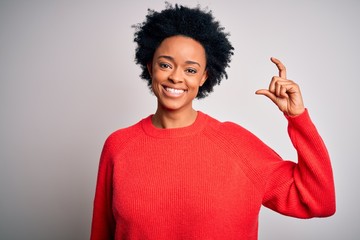 Young beautiful African American afro woman with curly hair wearing red casual sweater smiling and confident gesturing with hand doing small size sign with fingers looking and the camera. Measure