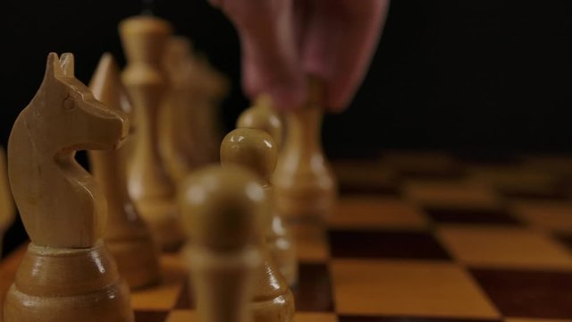 Human's hand makes first move by white pawn e2 e4 in chess game. Macro parallel dolly shot of wooden authentic chess. Two players gaming.