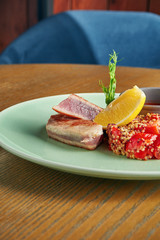 Grilled tuna steak with quinoa garnish with tomatoes and red sauce in a plate on a wooden background. Close up, selective focus