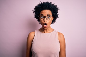 Fototapeta na wymiar Young beautiful African American afro woman with curly hair wearing t-shirt and glasses afraid and shocked with surprise expression, fear and excited face.