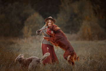 Beautiful long-haired blonde young woman in English style with Irish setter and Weimaraner dogs in...