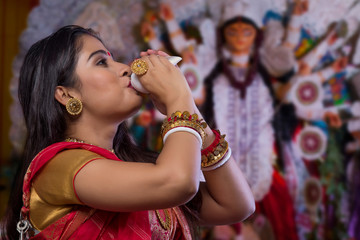 "Portrait of a beautiful Bengali woman blowing
conch shell at Durga puja"
