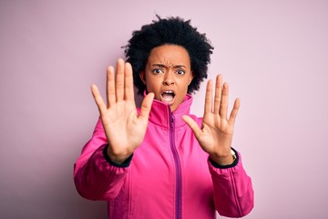 Young African American afro sportswoman with curly hair wearing sportswear doin sport afraid and terrified with fear expression stop gesture with hands, shouting in shock. Panic concept.