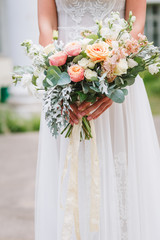 Beautiful wedding bouquet in hands of the bride. Trendy and modern wedding flowers. Woman in wedding dress outdoors. Fine art background.