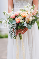 Beautiful wedding bouquet in hands of the bride. Trendy and modern wedding flowers. Woman in wedding dress outdoors. Fine art background.