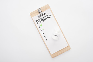 top view of clipboard with probiotics empty list and pills on white background