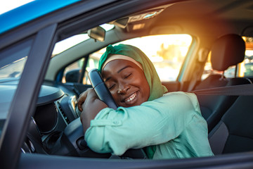 My First Car. Visiting car dealership. Beautiful woman is hugging her new car and smiling. Young...