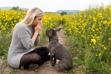 Young woman suffers from allergy in a rape field with her dog and has to sneeze