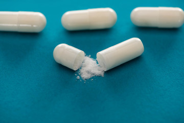 close up view of probiotic capsules with white powder on blue background
