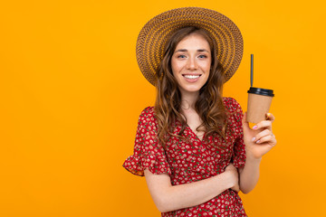portrait of charming stylish smiling girl in a hat with a paper cup on an orange background