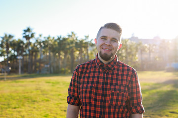 Obraz premium Handsome young smiling man standing on the grass at park. Summer in the city concept.