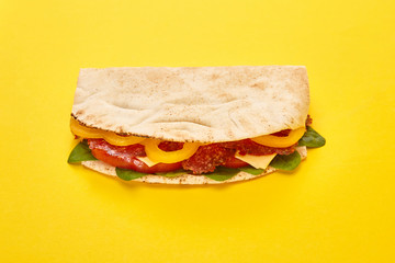 Obraz premium fresh sandwich with salami, pita, vegetables and cheese on yellow background