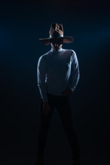 Fototapeta na wymiar Portrait of a sexy young man with cowboy hat posing in a studio on high contrast and dark background