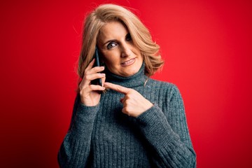Middle age beautiful blonde woman having conversation talking on the smartphone very happy pointing with hand and finger